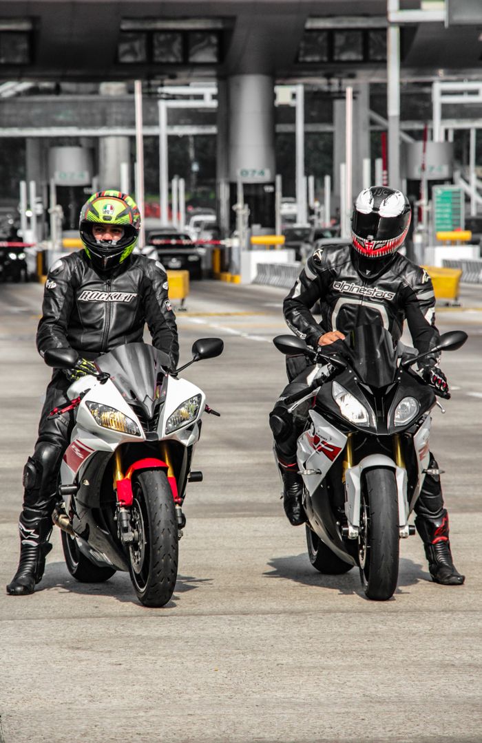 Two motorcyclists in full gear on sportbikes at an urban checkpoint.