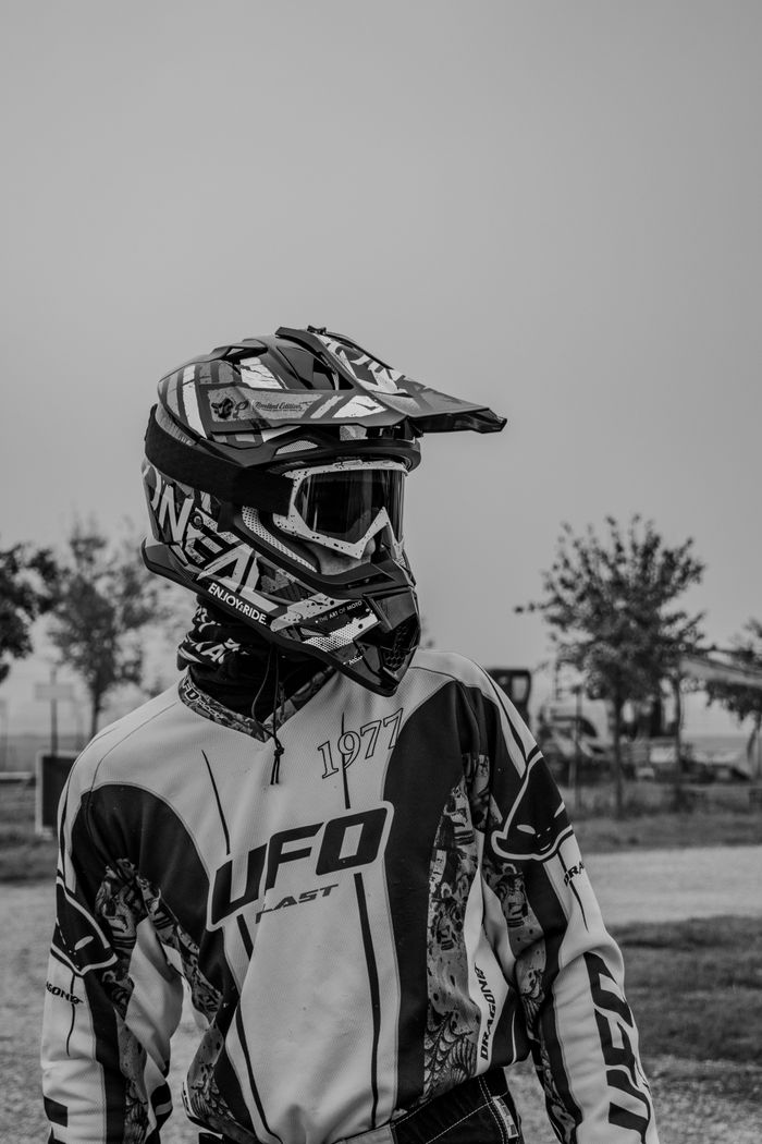 Motocross rider wearing gear and helmet in black and white outdoor setting.