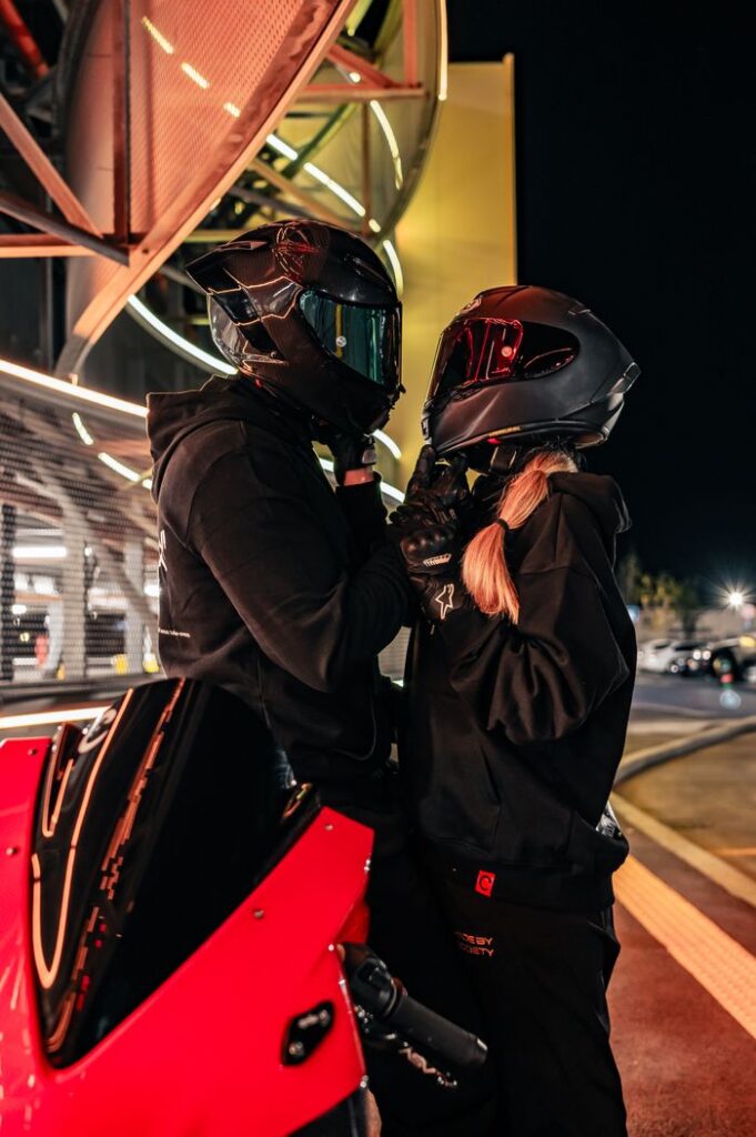 A romantic moment between two helmeted bikers at night in a modern urban setting.