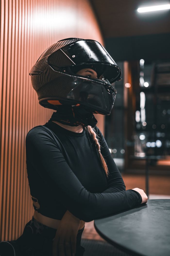why-choose-us-03 A woman wearing a black motorcycle helmet sits indoors with a reflective visor.