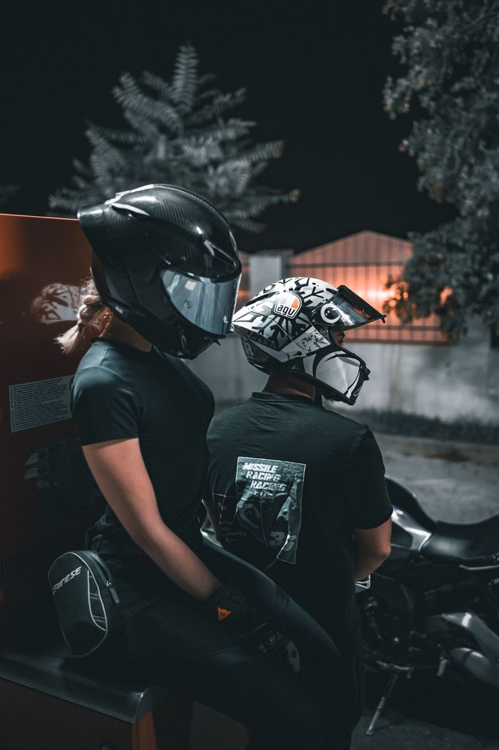 services-05 Two motorcyclists in helmets sitting on a motorcycle outdoors at night.