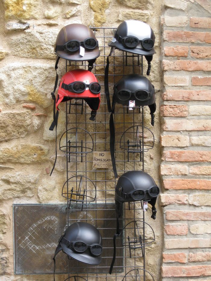 services-01 Six vintage style motorcycle helmets with goggles arranged on a metal rack against a rustic wall.