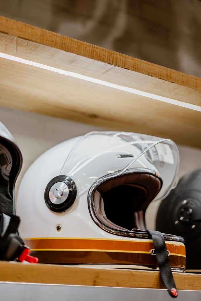 services-09 Close-up of a sleek white motorcycle helmet with visor on a wooden shelf, showcasing modern design.