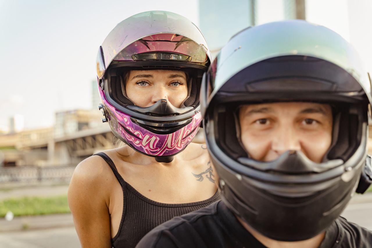 Close-up of two motorcyclists wearing helmets, showcasing city life and safety.