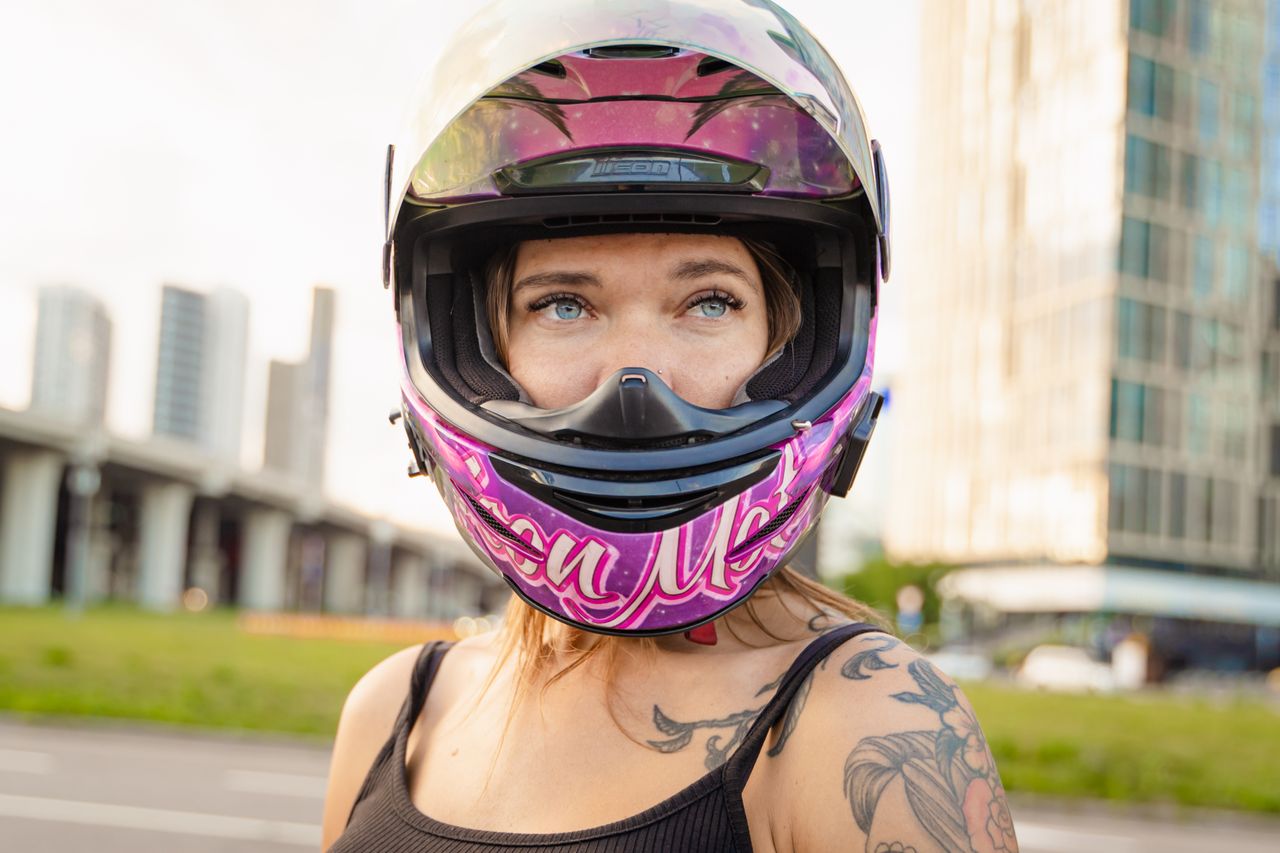 hero-02 Close-up of a woman with tattoos wearing a vibrant motorcycle helmet outdoors.